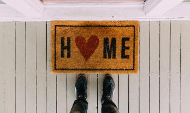 Two feet standing in front of a doormat that says Home