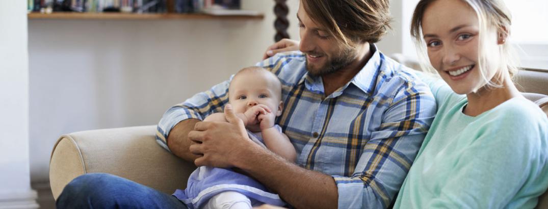 a young couple sitting on a couch, while the father holds their baby