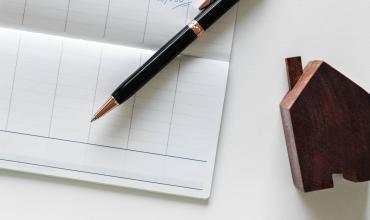 a checkbook, pen and wooden toy house on a table