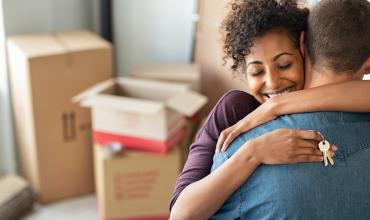 two people hugging in front of moving boxes holding a key