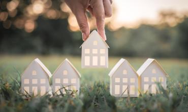 Paper houses being placed on the grass by a hand above