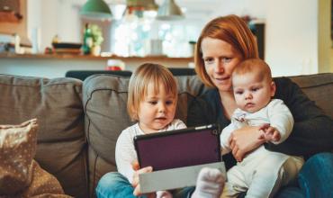 two kids and a woman looking at a tablet on a couch
