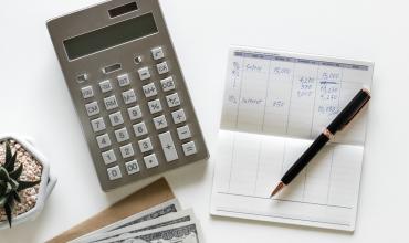 a table with a calculator, checkbook and pen