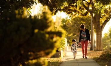 a woman and a boy holding hands walking down a sidewalk