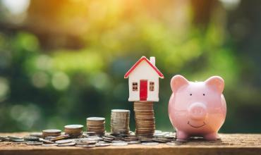 Should I Refinance My Mortgage? Learn the Basics First Coins stacked up with a house on top of them and a piggy bank to the right