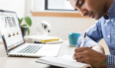 Man sitting in front of computer writing in a journal