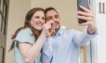 New homeowners taking a selfie holding up a key to their new home