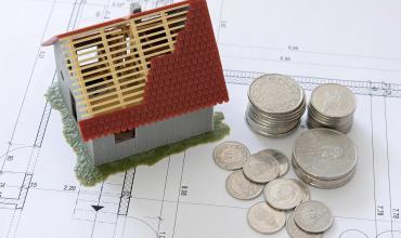 How Your Credit Score Impacts Your Home Buying Journey A miniature house with a roof being built next to some change on top of home plans