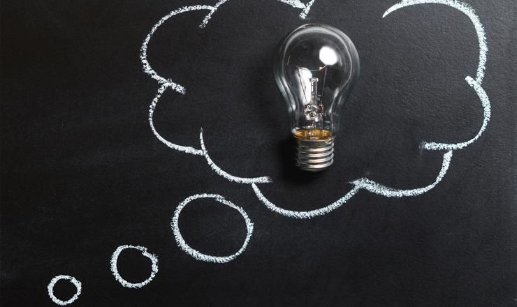 A light bulb in a drawing of a thought cloud on a chalkboard