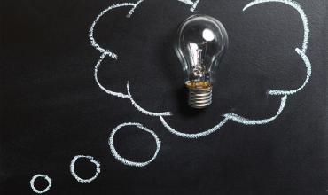 A light bulb in a drawing of a thought cloud on a chalkboard