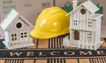 A hardhat sitting between two miniature houses on a welcome mat