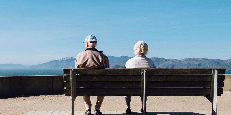 Older couple sitting on a bench facing mountains