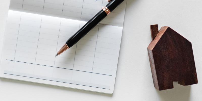 a checkbook, pen and wooden toy house on a table