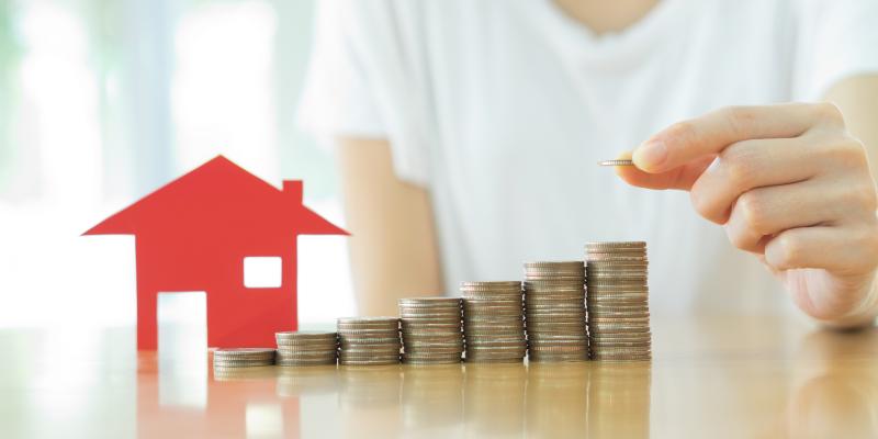 an individual stacking coins next to a small model home