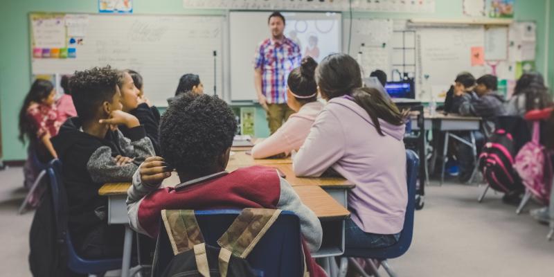 Kids in a classroom with a teacher in front of the dry erase board