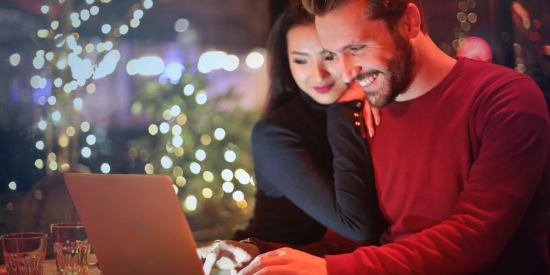 Couple looking at computer screen, with Christmas tree in background