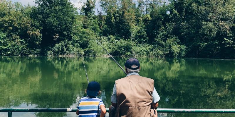 A man and a small boy fishing together seen from the back