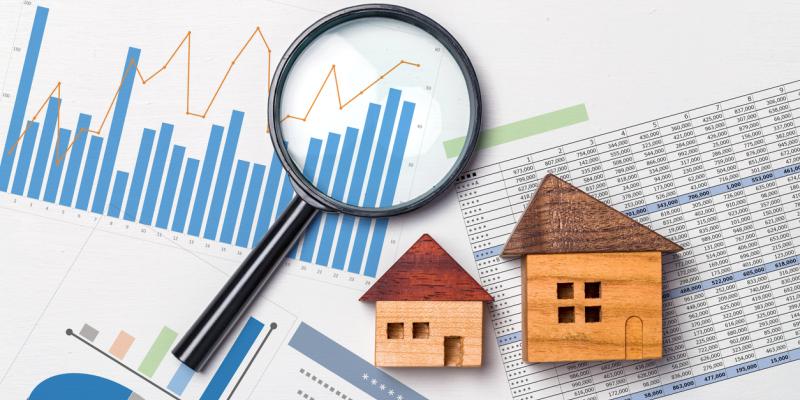 A magnifying glass over charts.  Two toy wooden houses