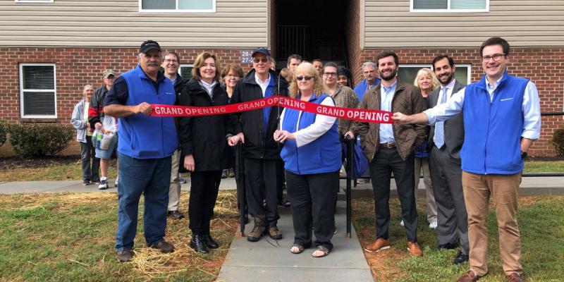 A group of people cutting a ribbon outside of the apartment development