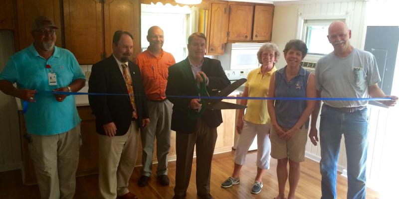 group of people around a ribbon getting ready to cut it inside a home