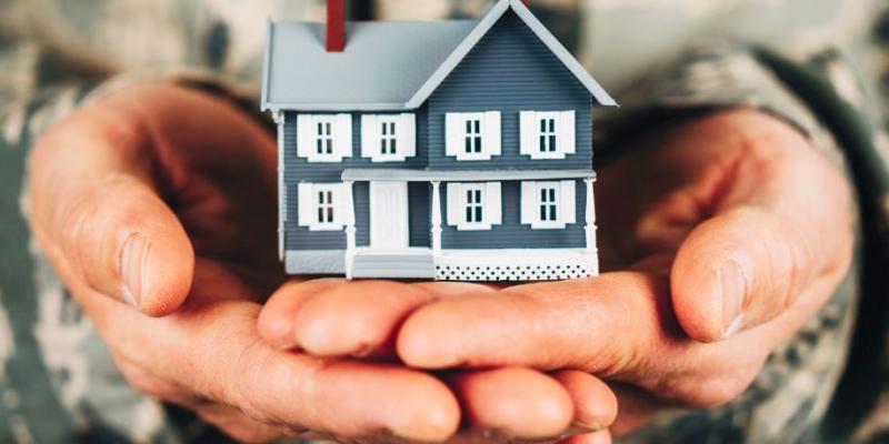 Person in a military uniform holding a little blue house