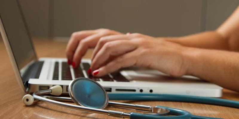 A stethoscope laying next to a person typing on a computer