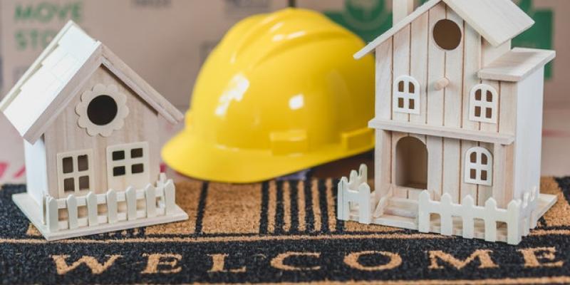 A hardhat sitting between two miniature houses on a welcome mat